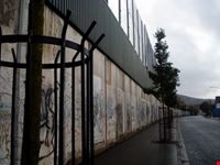Il muro tappezzato di scritte e sovrastato da ulteriori barriere